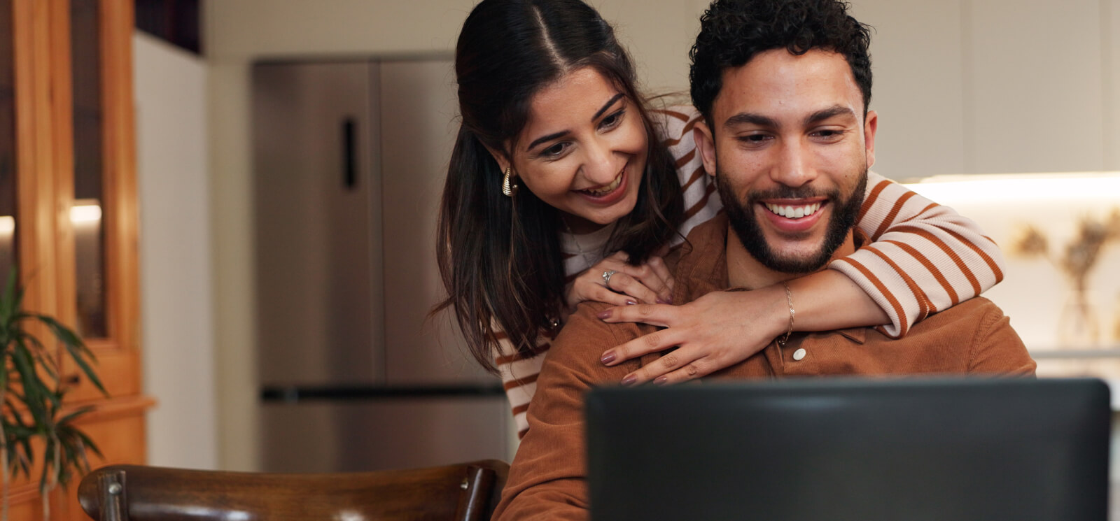 Happy couple look at computer screen in home kitchen